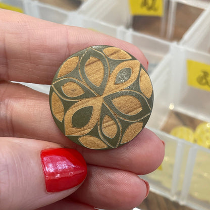 Hand holding a decorative button with a pattern, against a background of a button organizer.