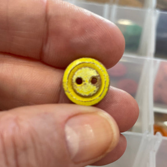Yellow button held between fingers with a container of buttons in the background