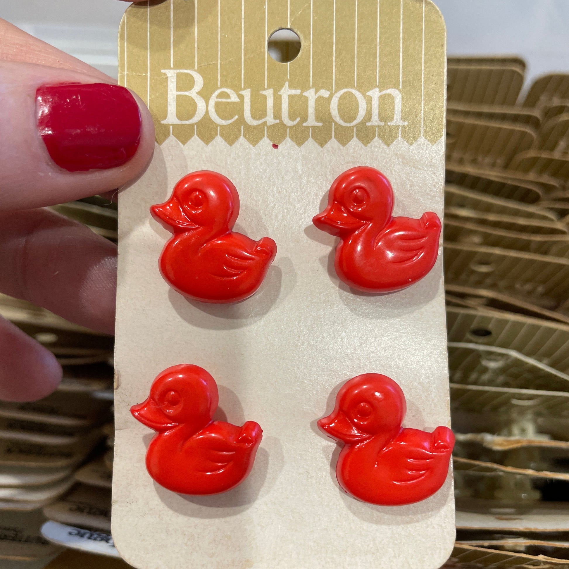 Red duck-shaped buttons on a Beutron card held by a hand with red nail polish.