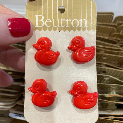 Red duck-shaped buttons on a Beutron card held by a hand with red nail polish.