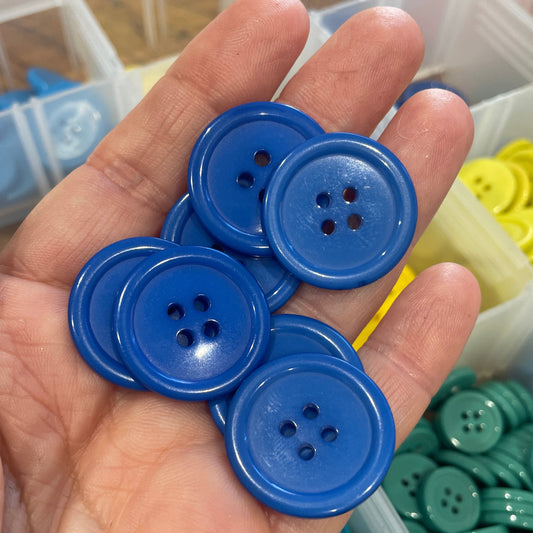 Hand holding blue buttons with a container of buttons in the background