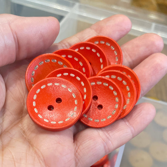 Hand holding red buttons with a container of buttons in the background