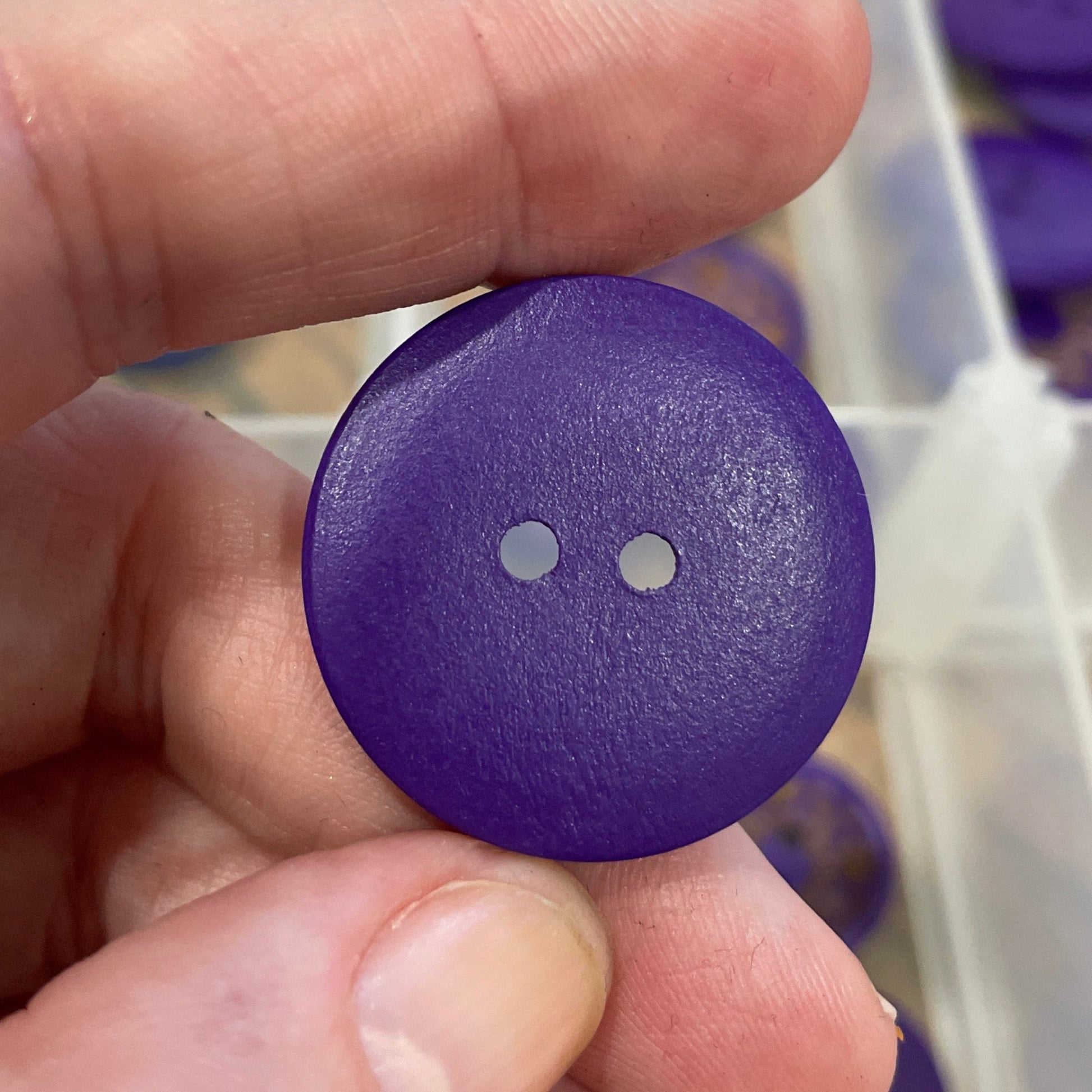 Purple button held by a hand with a clear container of buttons in the background