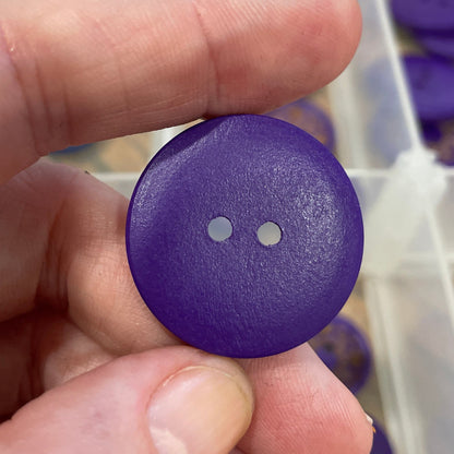 Purple button held by a hand with a clear container of buttons in the background