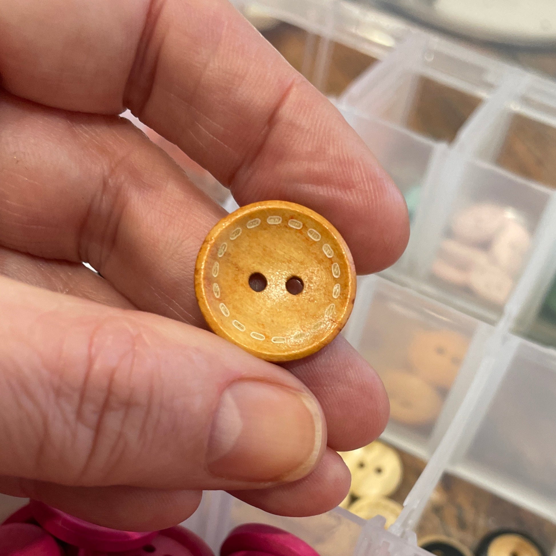 Hand holding a yellow button with a container of colorful buttons in the background