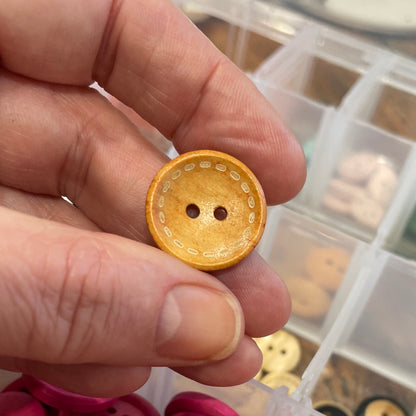 Hand holding a yellow button with a container of colorful buttons in the background