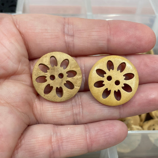 Gold decorative buttons held in a hand with a container of green buttons in the background.