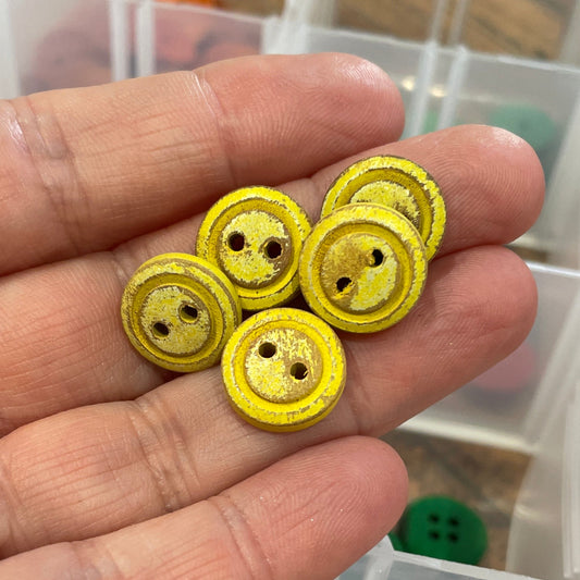 Hand holding yellow buttons with a container of buttons in the background