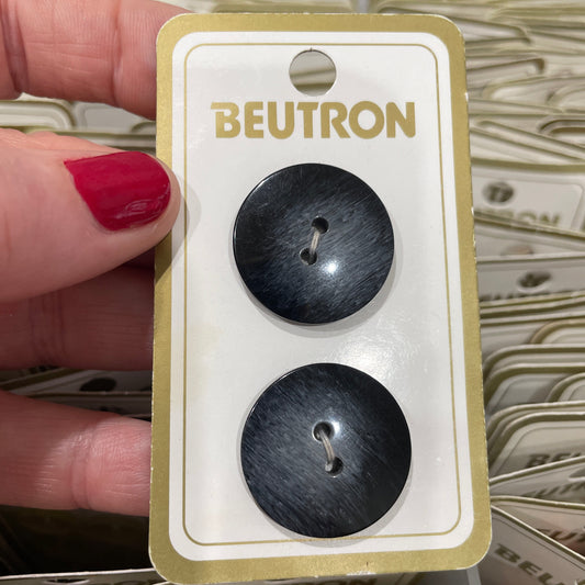 Two black buttons on a Beutron branded card held by a hand with red nail polish.