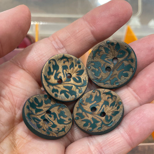 Hand holding four decorative buttons with intricate designs, with a blurred background of more buttons.