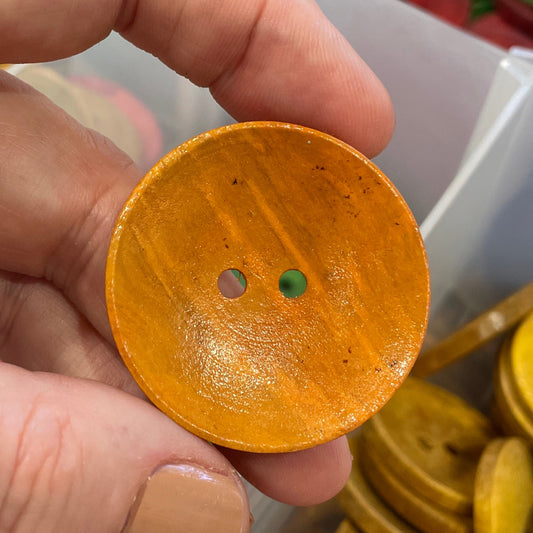 Hand holding a wooden button with a container of buttons in the background