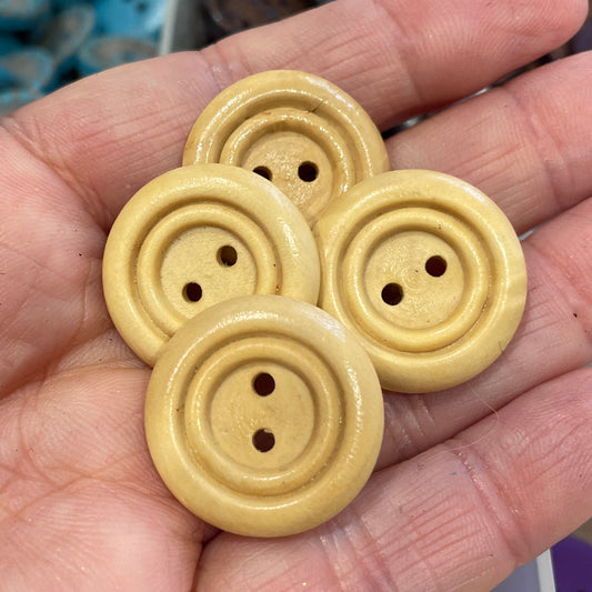 Hand holding four beige buttons with a blurred background of more buttons.