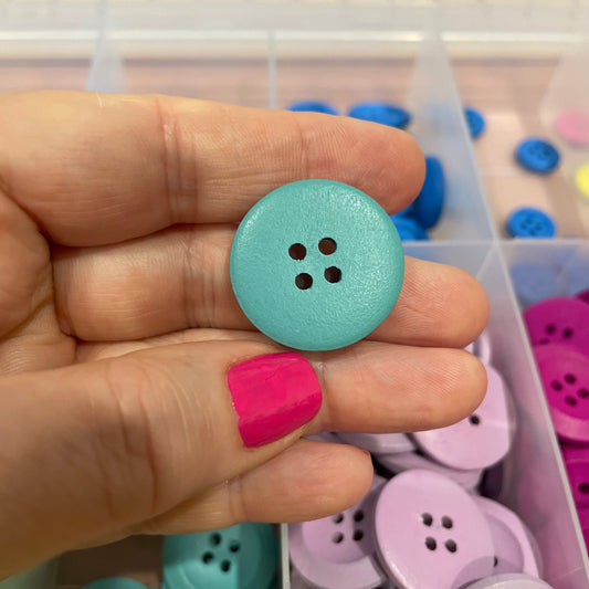 Hand holding a light blue button with a container of colorful buttons in the background