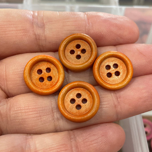 Hand holding four wooden buttons with a container of buttons in the background