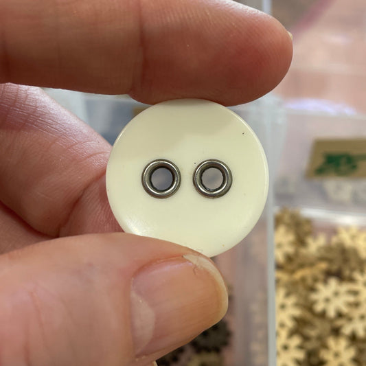 Hand holding a white buttons, with a container of buttons in the background.