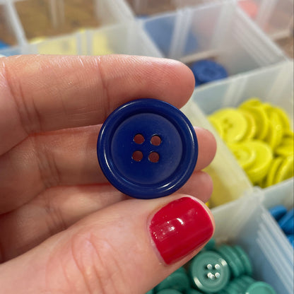 Hand holding a blue button with a container of buttons in the background