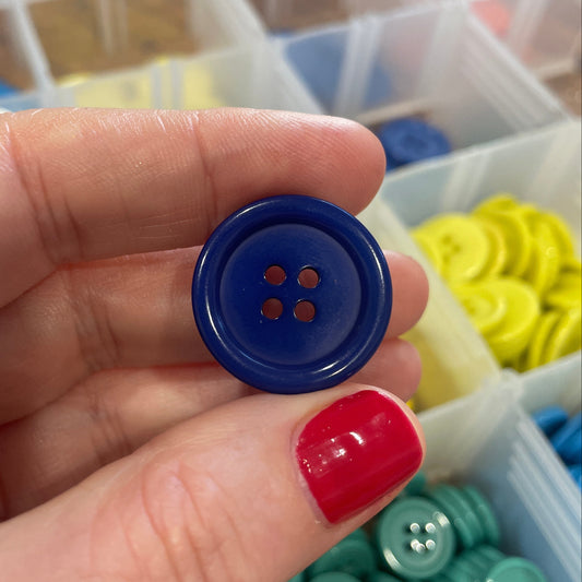 Hand holding a blue button with a container of buttons in the background