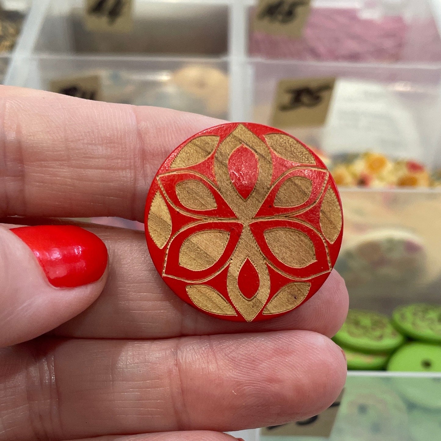 Hand holding a red decorative button with a clear container of buttons in the background