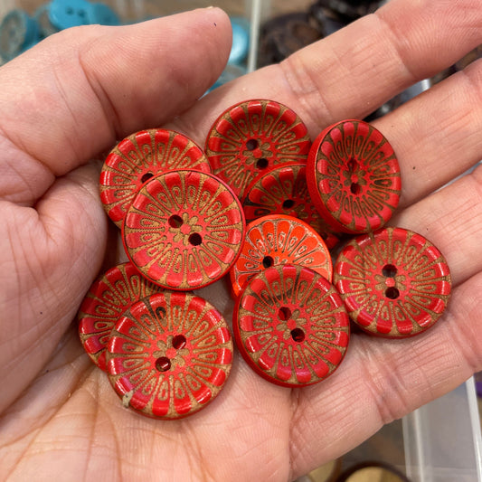Hand holding red buttons with gold patterns against a blurred background
