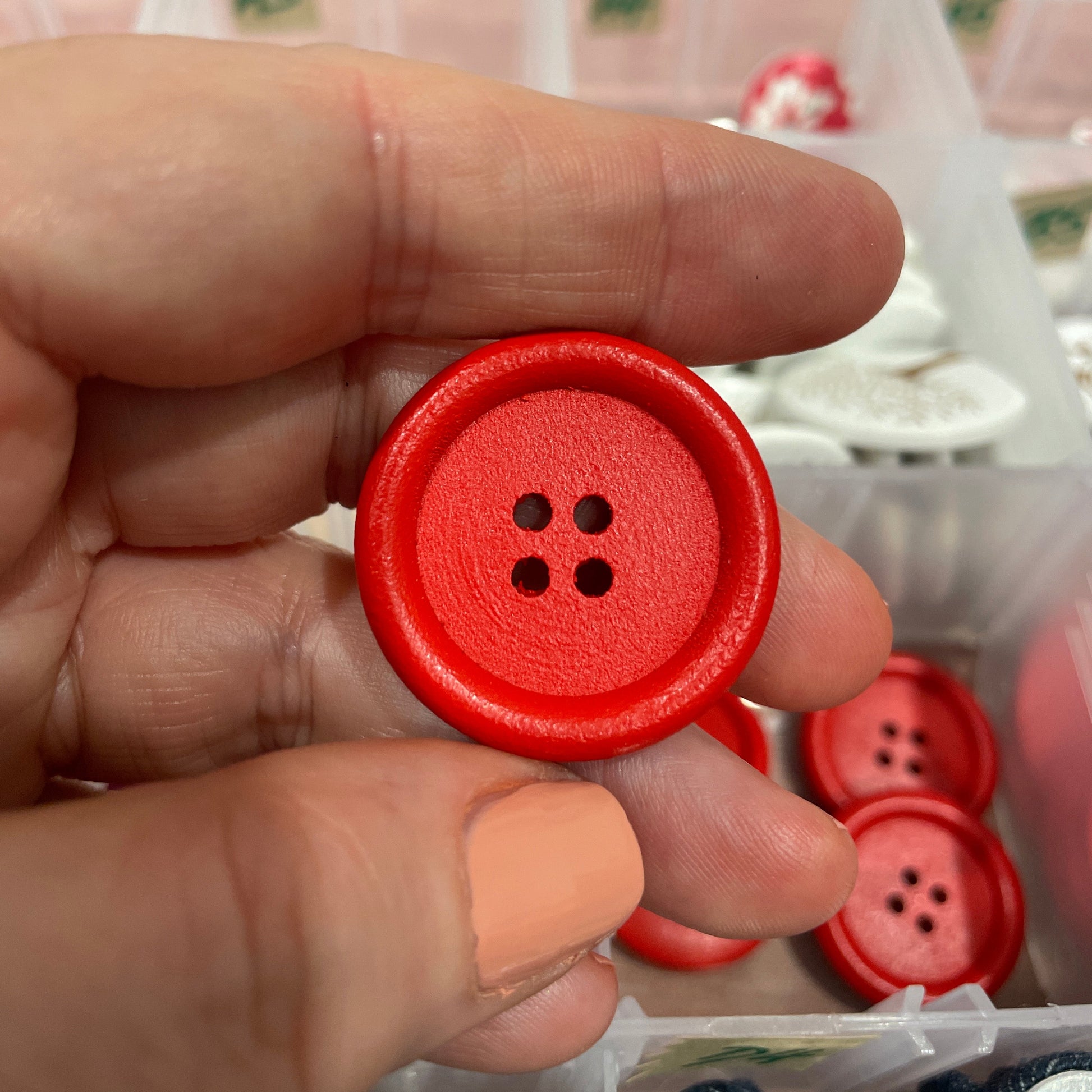 Hand holding a red button with a blurred background of more buttons and a box.