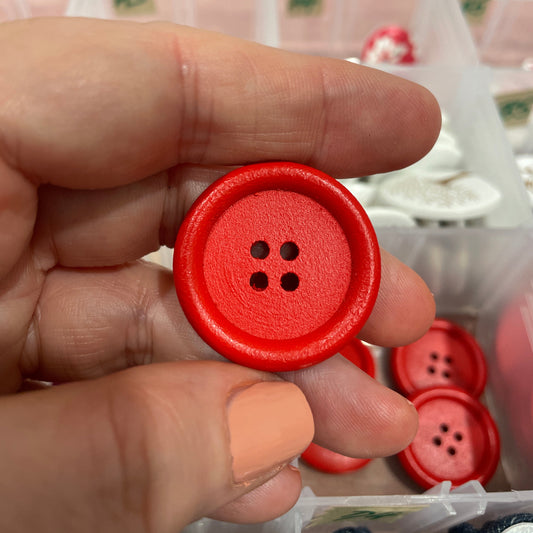 Hand holding a red button with a blurred background of more buttons and a box.