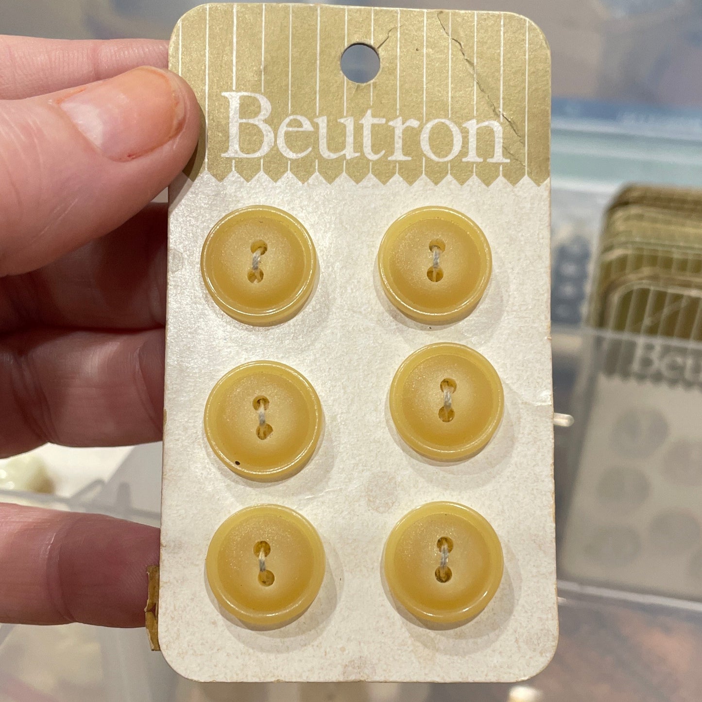 Hand holding a card with six yellow buttons, branded 'Beulon', against a blurred background.