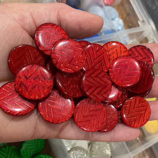 Hand holding red decorative buttons with a container of various buttons in the background.