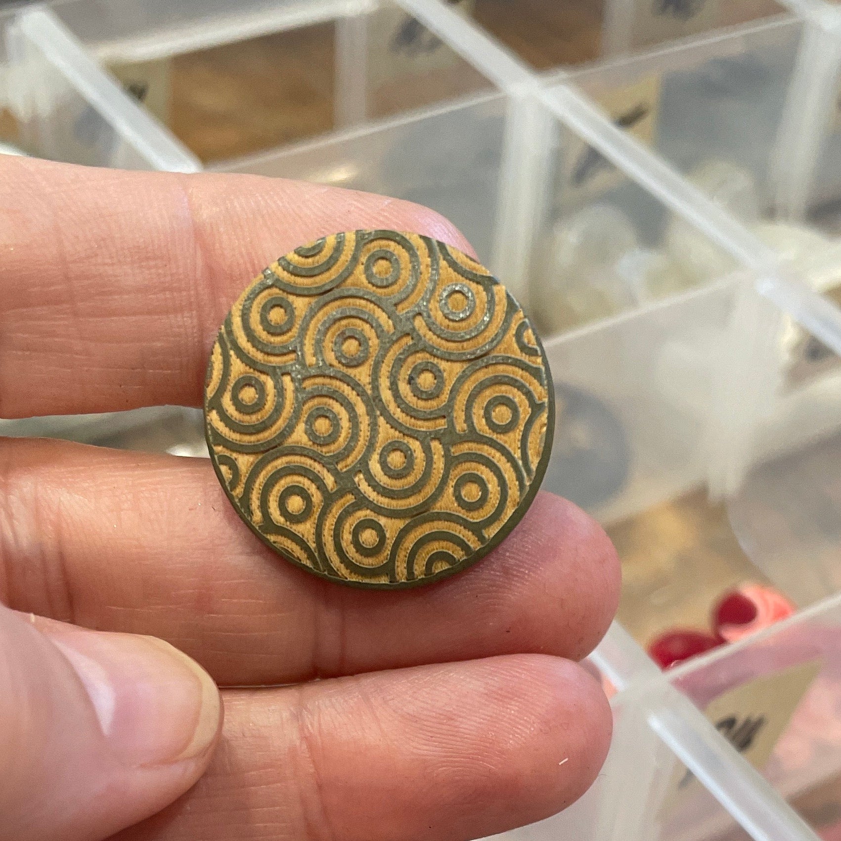 Hand holding a button, against a blurred background of a storage box.