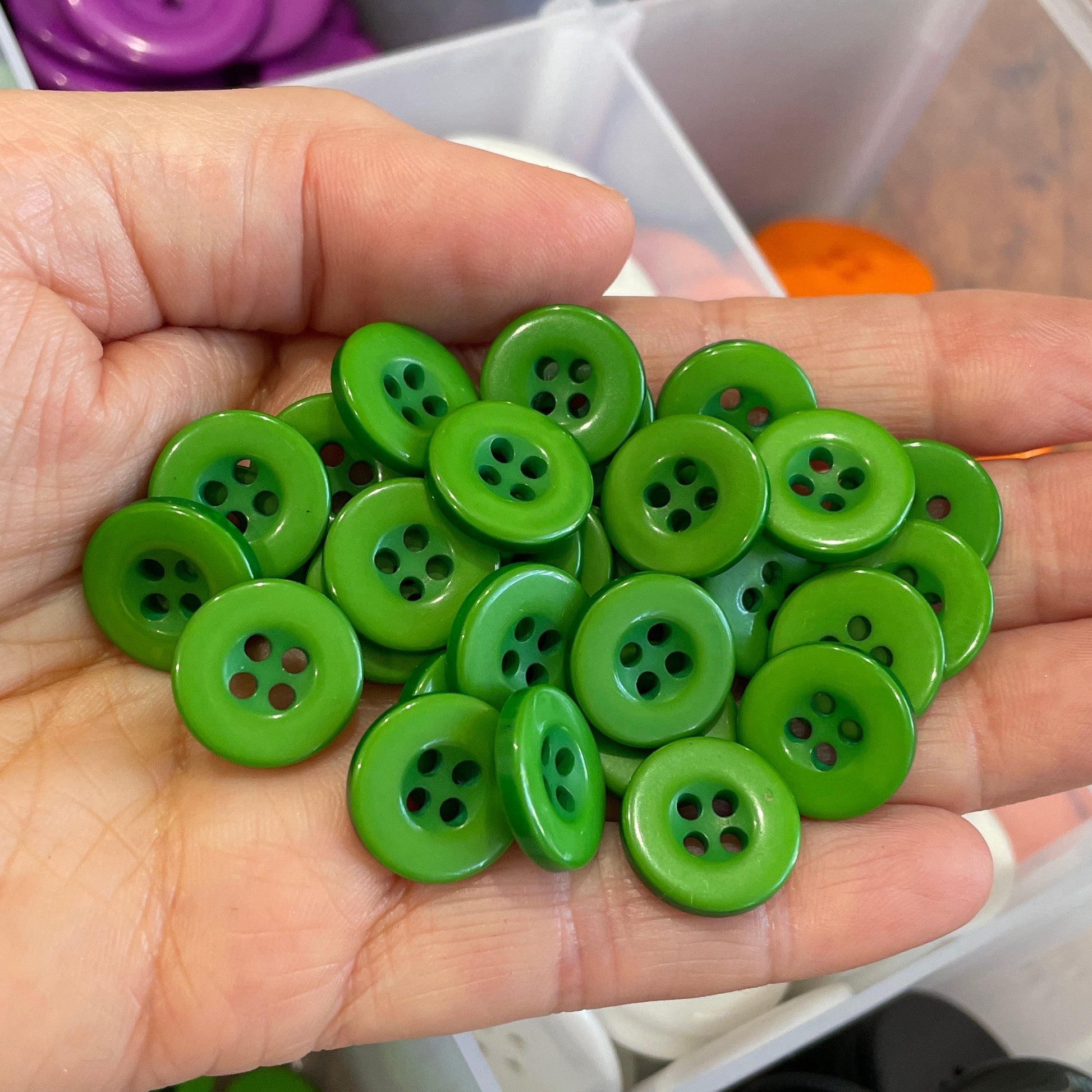 Hand holding green buttons with a container of assorted buttons in the background