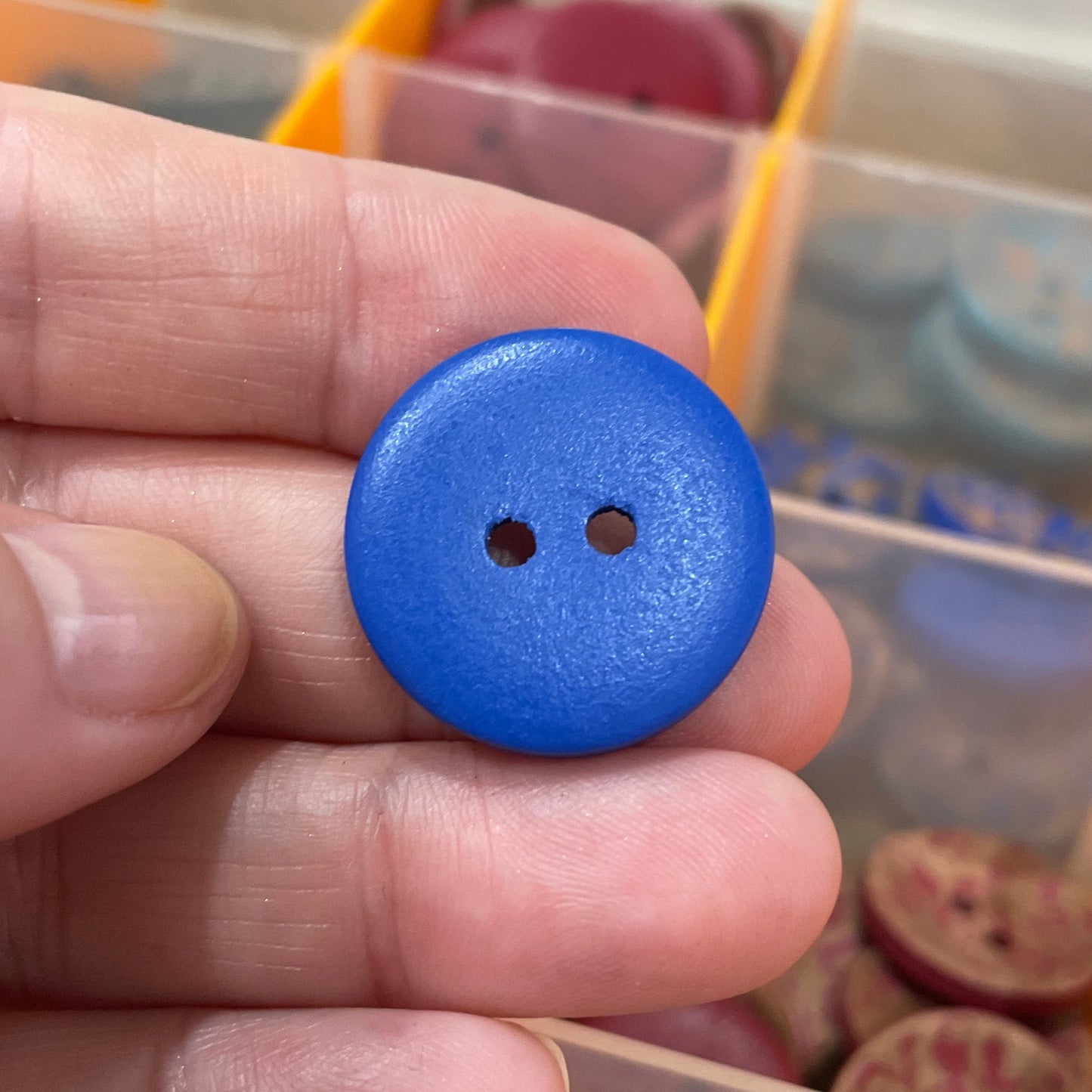 Blue button held between fingers with a container of buttons in the background