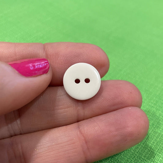 Small white button held between fingers on a green fabric background