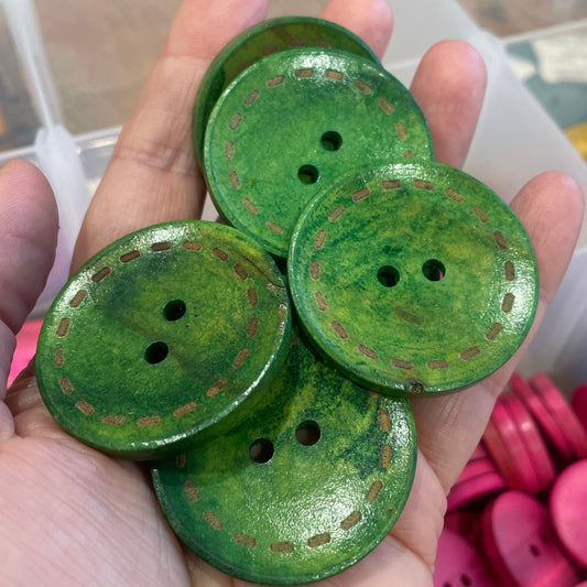 Green buttons held in a hand with a container of pink buttons in the background
