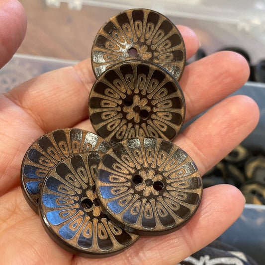 Hand holding three decorative buttons with intricate designs, blurred background
