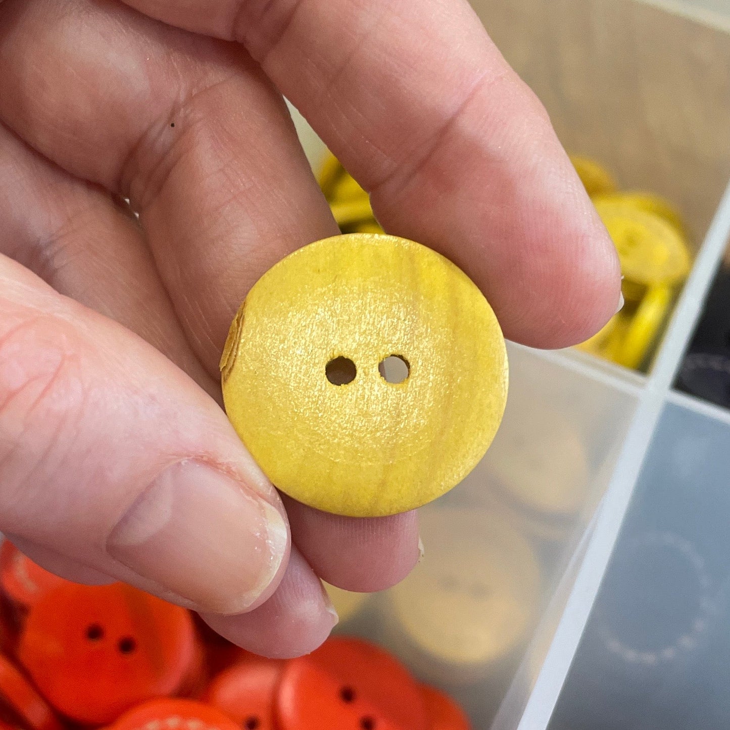 Hand holding a yellow button with a container of orange buttons in the background