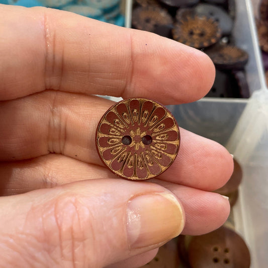 Hand holding a wooden button with a blurred background of button assortment