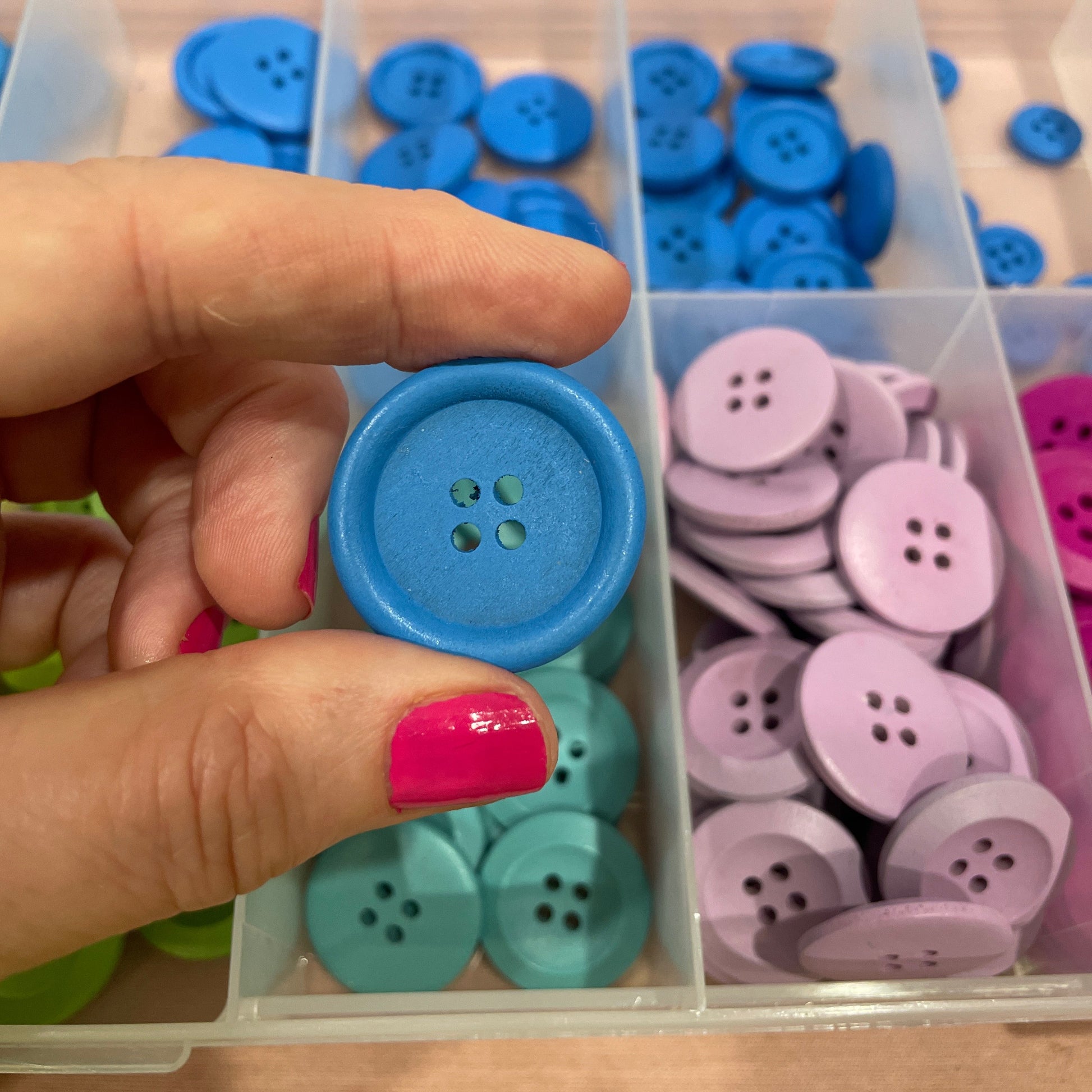 Colorful buttons in a clear container with a hand holding a blue button.
