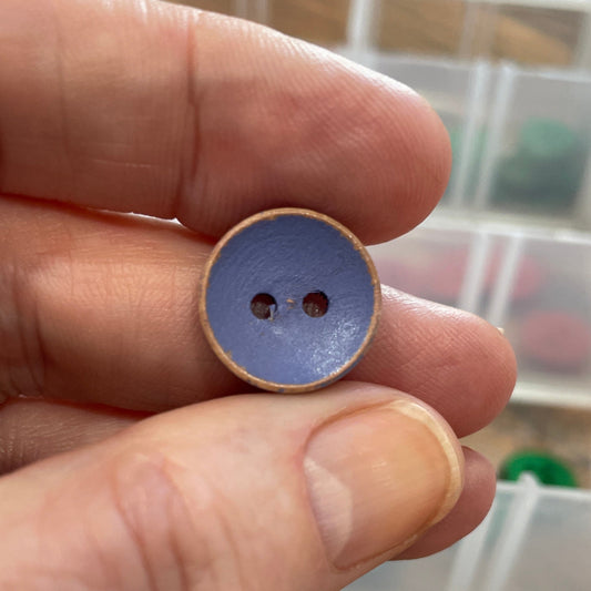 Hand holding a small blue button with a clear container of buttons in the background