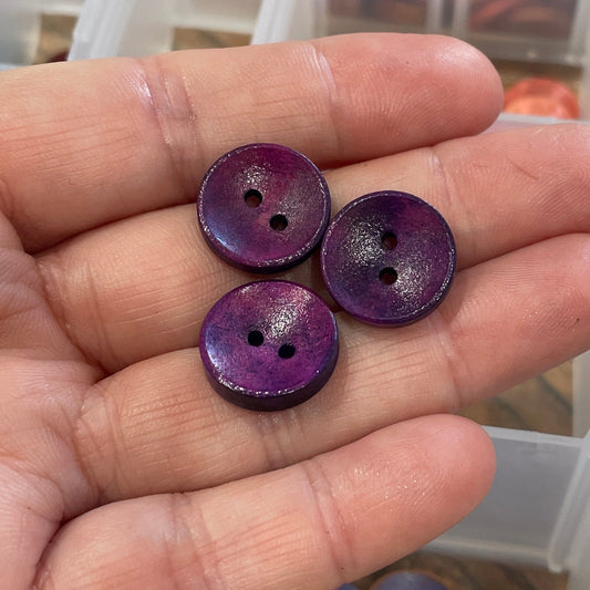 Hand holding purple buttons with a container of buttons in the background