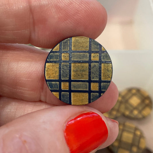 Hand holding a round button with a checkered pattern, surrounded by other buttons in the background.
