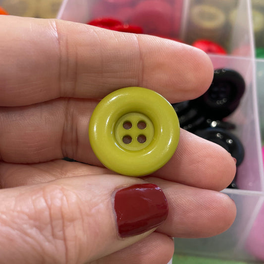 Hand holding a yellow button with a background of colorful buttons in a box