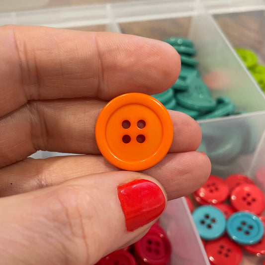 Hand holding an orange button with a container of colorful buttons in the background
