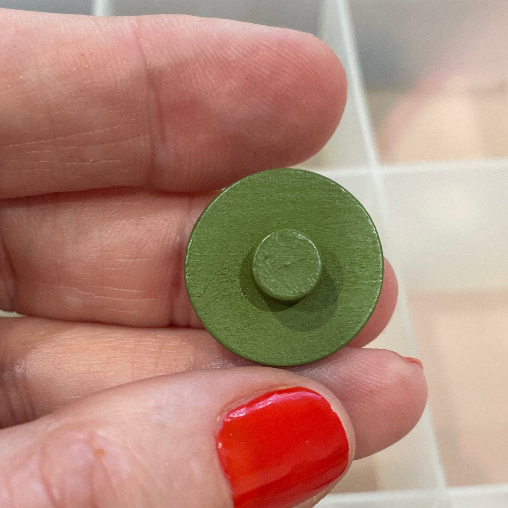 Hand holding a green button with a container of buttons in the background