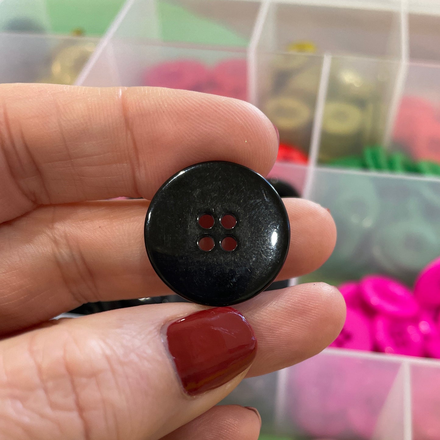 Black button held by a hand with a colorful assortment of buttons in the background