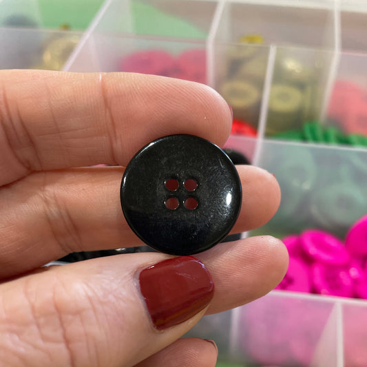 Black button held by a hand with a colorful assortment of buttons in the background