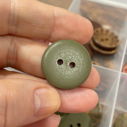 Hand holding a green button with a collection of buttons in the background