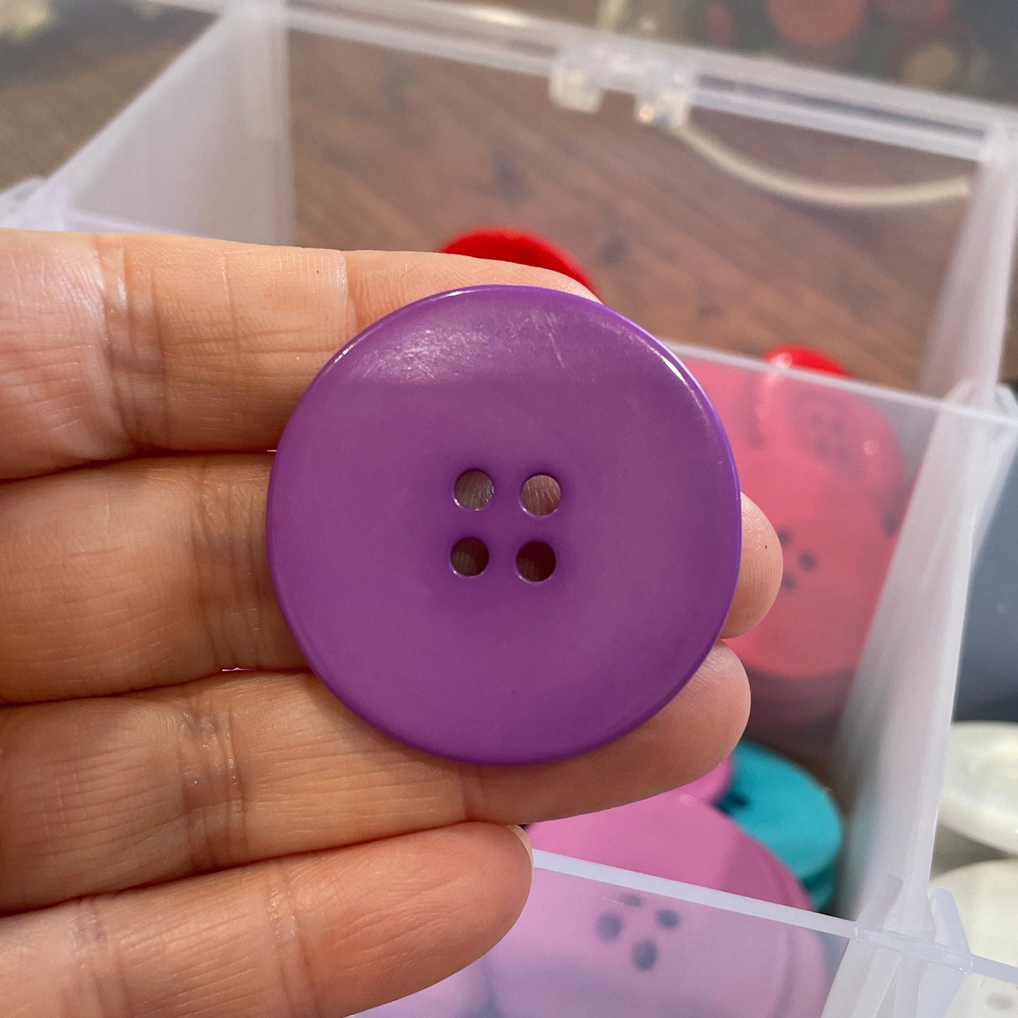 Purple button held in hand with container of buttons in the background