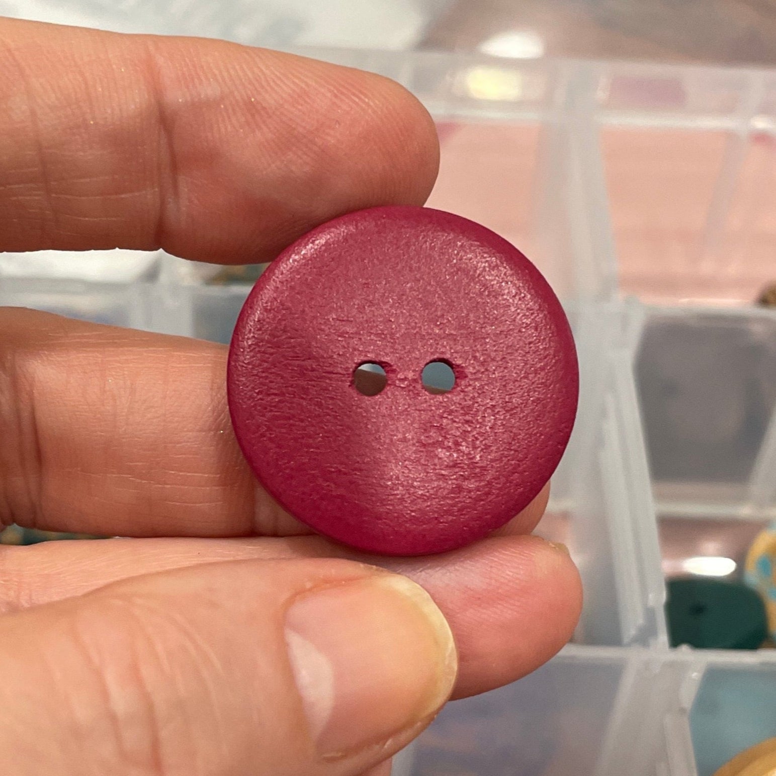 Hand holding a red button with a clear container of buttons in the background