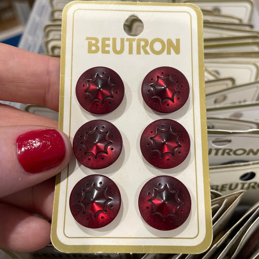 Card with six red buttons held by a hand with red nail polish, against a blurred background of similar cards.