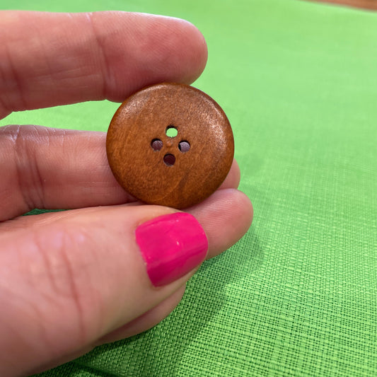 Wooden button held between fingers against a green background