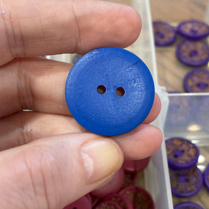 Hand holding a blue button with a collection of buttons in the background.